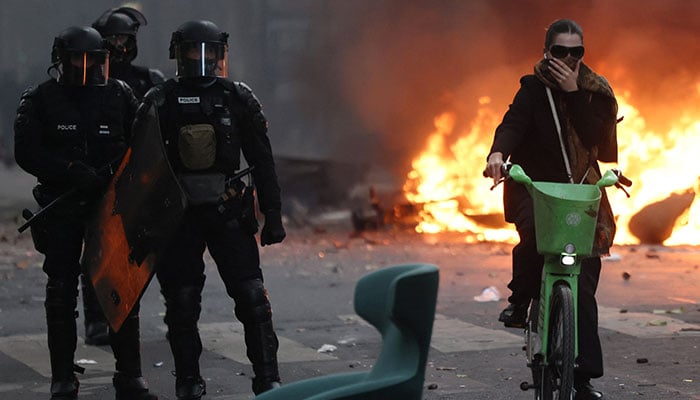 A woman rides a bicycle past French riot police standing near a burning barricade amid clashes with protesters during a day of demonstrations against the cost of living and rising fuel prices in Paris, France, October 17, 2026. — Reuters