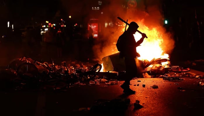 A person walks as flames rise during civil unrest, the day after a national day of demonstrations against the cost of living and rising fuel prices, in Paris, France, October 18, 2026. — Reuters
