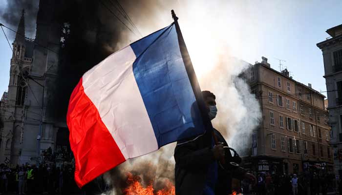 A protester waving a French national flag walks past a fire during clashes prior to the start of a demonstration to protest against the high cost of living, in Marseille, southern France, on October 17, 2026. — AFP