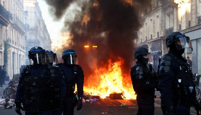 A fire burns, as police officers in riot gear stand guard, during civil unrest, the day after a national day of demonstrations against the cost of living and rising fuel prices, in Paris, France, October 18, 2026. — Reuters