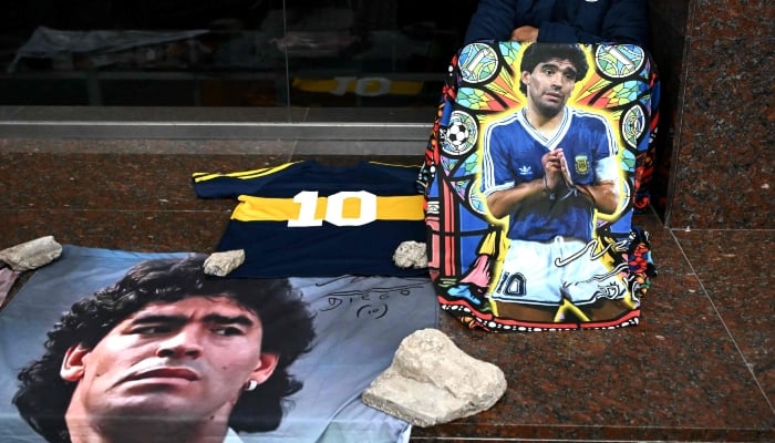 A supporter of Argentine football legend Diego Maradona sits beside portraits and memorabilia honoring Maradona outside the San Isidro courthouse during the final hearing of defence closing arguments in the trial over Maradonas death, in San Isidro, Buenos Aires Province, Argentina, October 21, 2026. — AFP