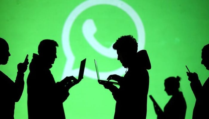 Silhouettes of laptop and mobile device users are seen next to a screen projection of Whatsapp logo in this picture illustration taken March 28, 2018. — Reuters