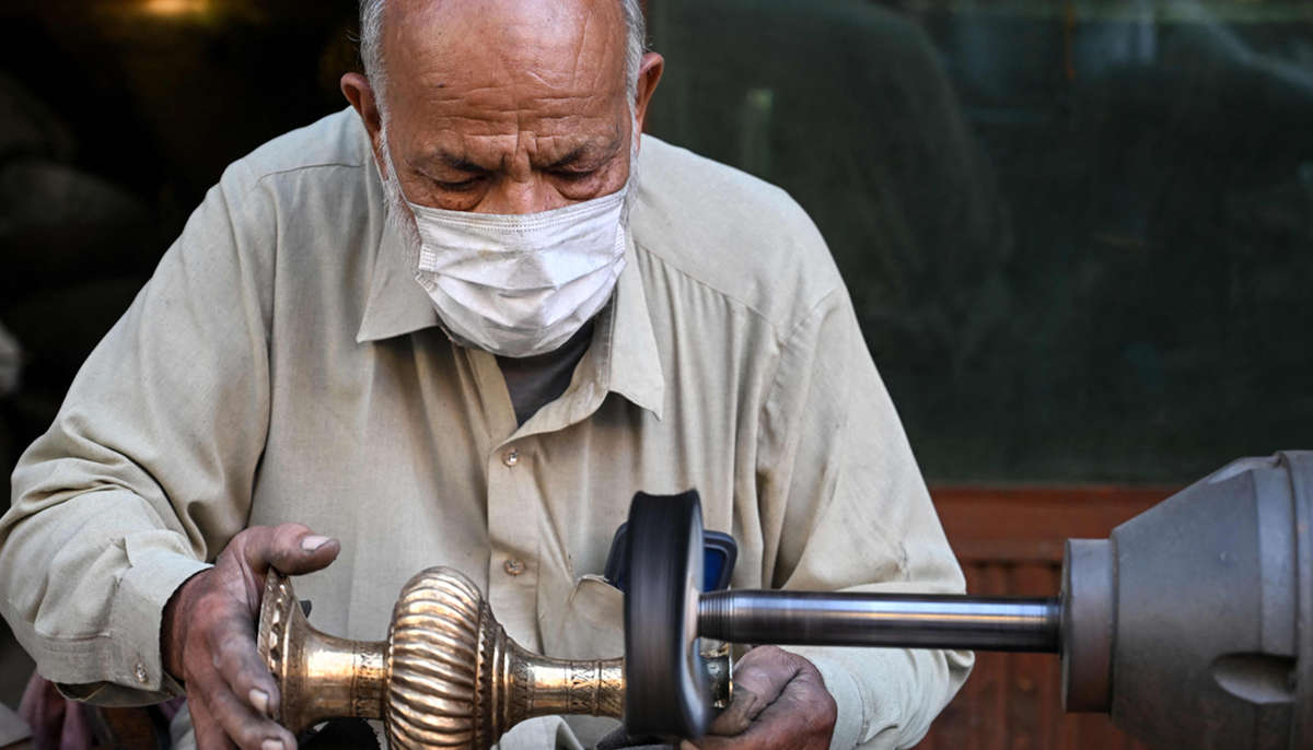 Antique dealer Ahsan Shakeel polishes an artefact outside his shop, selling vintage items in Rawalpindi on October 20, 2026. — AFP