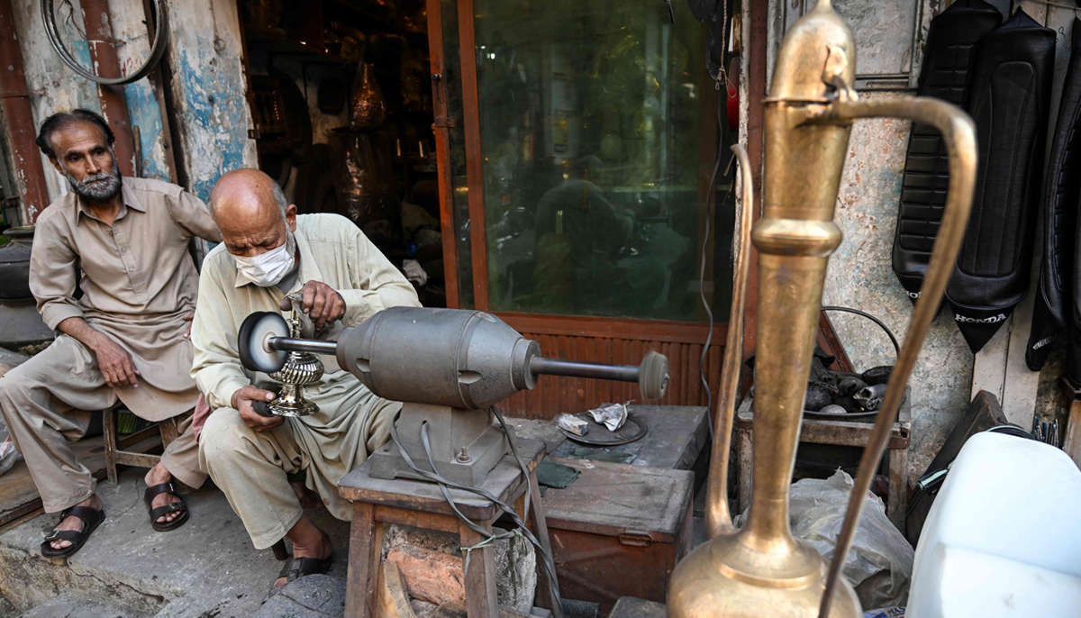 Antique dealer Ahsan Shakeel polishes an artefact outside his shop selling vintage items in Rawalpindi on October 20, 2026.— AFP