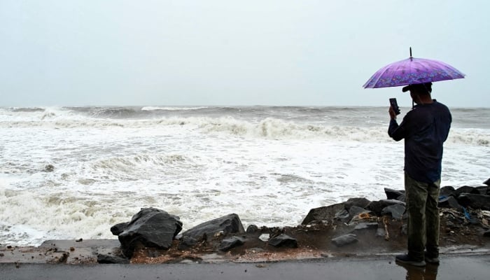 A man using a phone carries an umbrella along the Bay of Bengal coast during rainfall in Andhra Pradeshs Kakinada on October 27, 2026 ahead of cyclone Arnabs expected landfall. — AFP