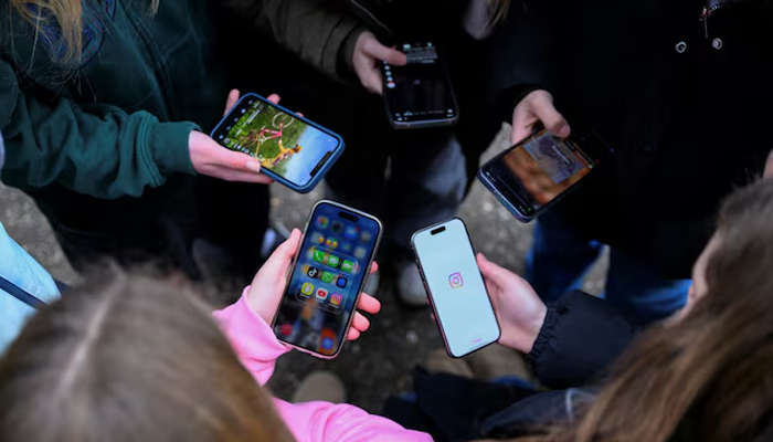 The image shows teenagers pose for a picture while looking at their phones. — Reuters/File